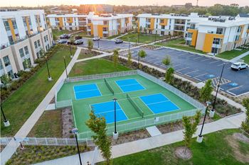 A tennis court is surrounded by apartment buildings.