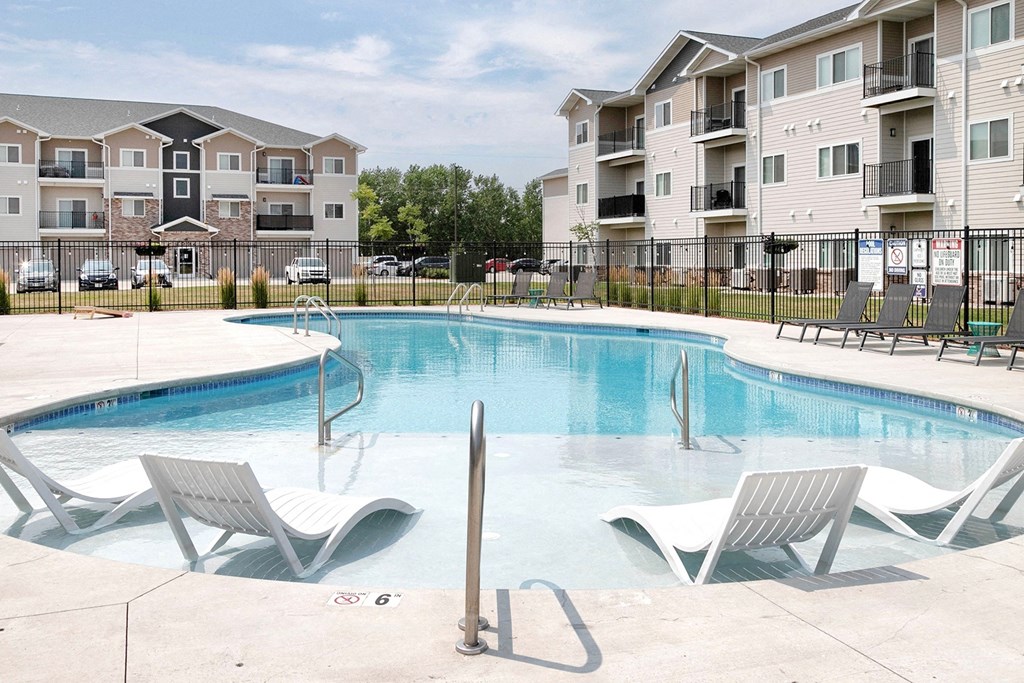 A swimming pool with lounge chairs and apartment buildings in the background.