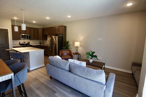 A modern living room with a grey couch and a kitchen in the background.