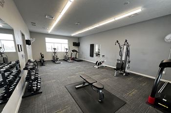 A gym with a variety of equipment including dumbbells, weight machines, and a bench press.