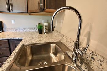 A kitchen sink with a chrome faucet and a marble countertop.