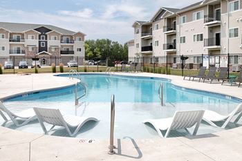 A swimming pool with lounge chairs and apartment buildings in the background.