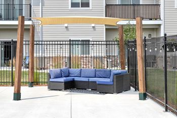 A blue couch is placed on a patio with a black fence.