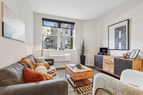 A living room with a grey couch, a wooden coffee table, and a large window.