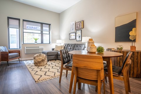 A living room with a grey couch, a wooden table and chairs, and a rug with a zigzag pattern.