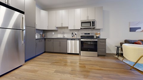 A modern kitchen with a refrigerator on the left and a dining area with a chair and table on the right.