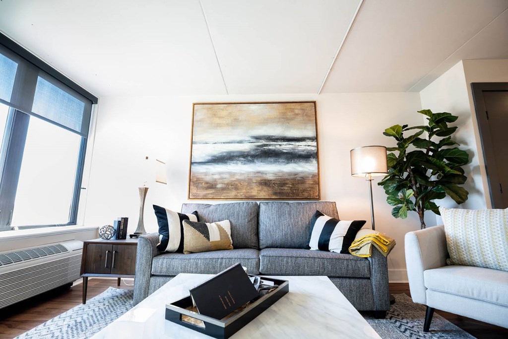 A living room with a grey couch, a painting on the wall, and a coffee table with a black box on it at Cityplace Apartment Homes Apartments, Pennsylvania