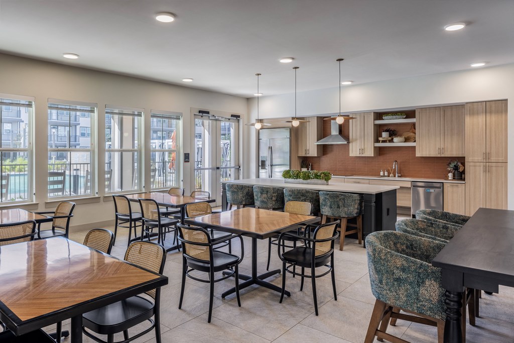 a dining area with tables and chairs and a kitchen with a large island and windows