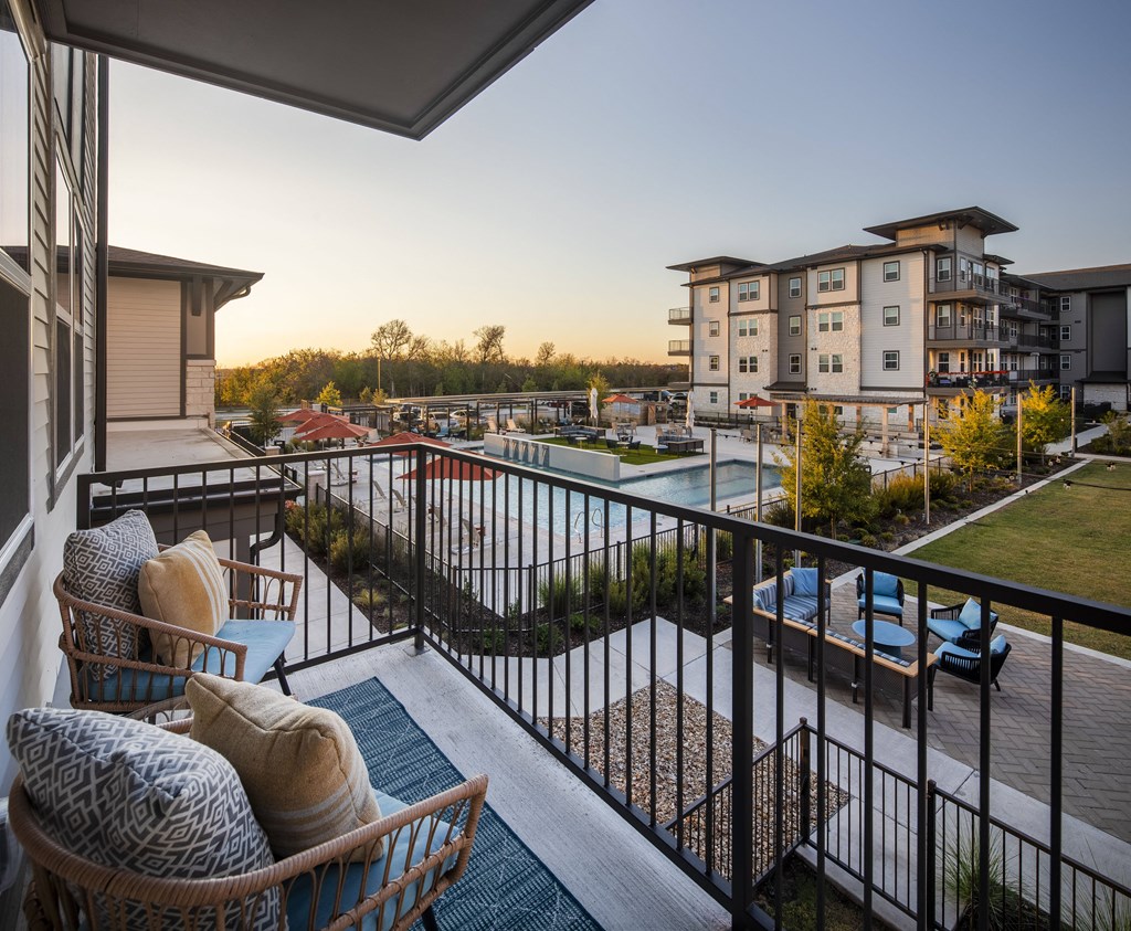 a balcony with a couch and chairs overlooking a pool and an apartment building