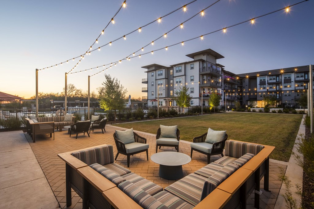 a patio area with chairs and tables and a lawn with a building in the background