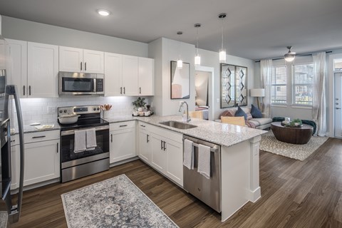 a kitchen and living room with white cabinets and stainless steel appliances at a senior apartment community