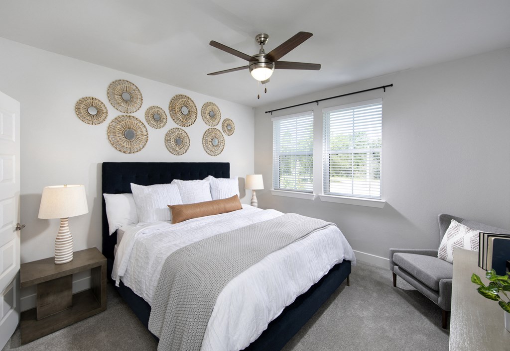 a bedroom with a queen-sized bed, ceiling fan, and windows at a senior apartment community