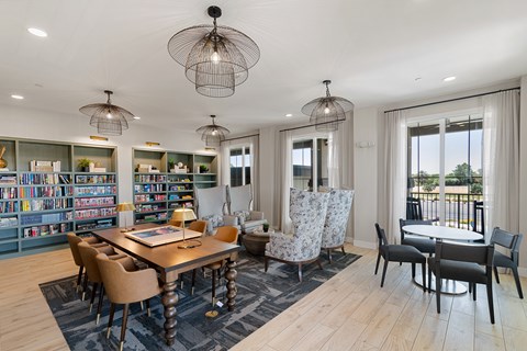 A well-lit room with a dining table surrounded by chairs and a bookshelf filled with books.