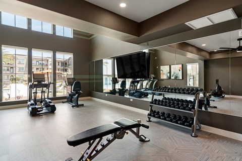 A gym with a variety of equipment including dumbbells, weight machines, and a flat screen TV.