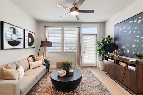 A living room with a beige couch, a black coffee table, and a flat screen TV mounted on the wall.