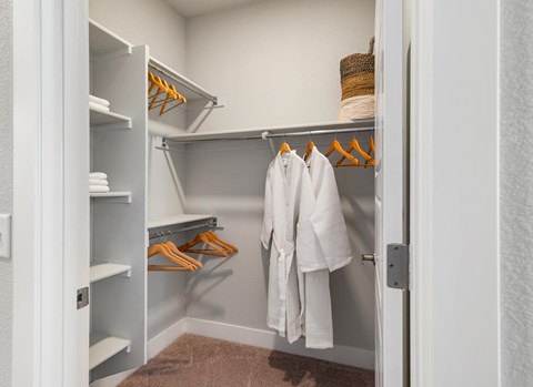 A white closet with clothes hanging and shelves.