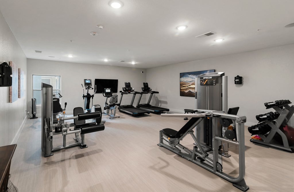 a gym with cardio equipment and weights on a wooden floor