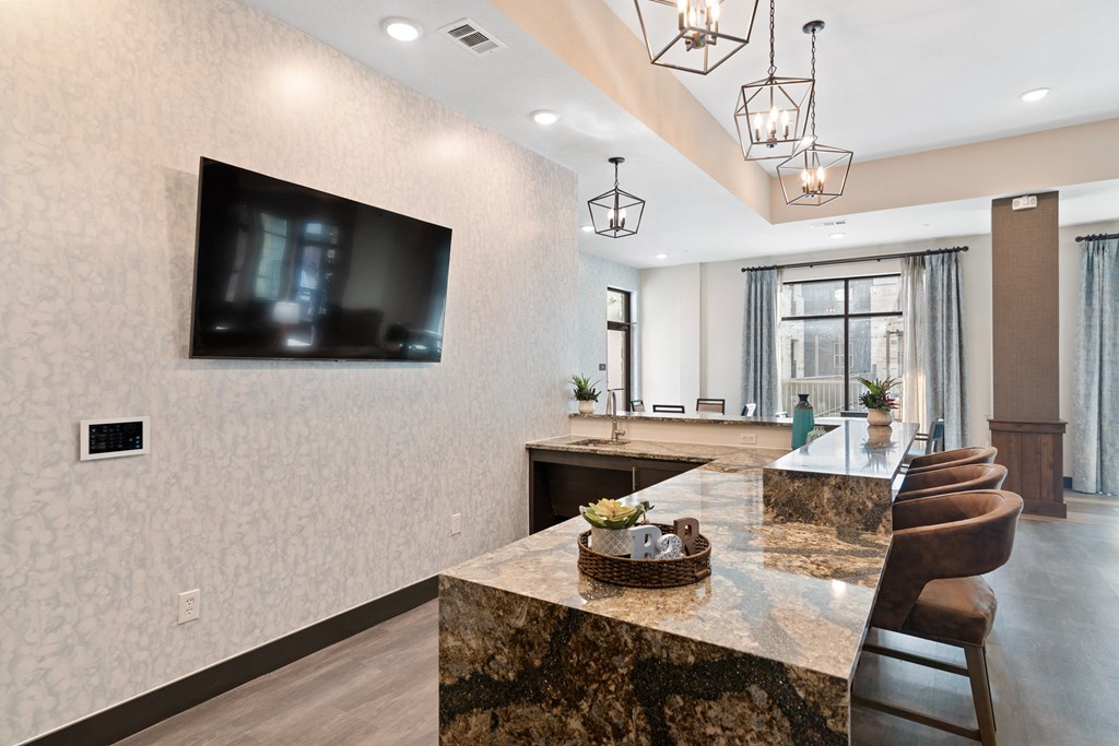 the kitchen has a large island with a granite countertop and a large tv on