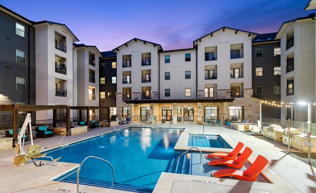 an apartment swimming pool with red chairs at dusk
