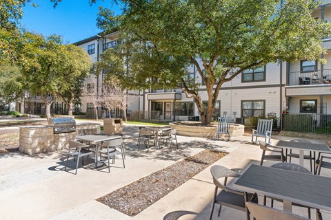 a patio with tables and chairs under shaded under trees at a senior apartment community