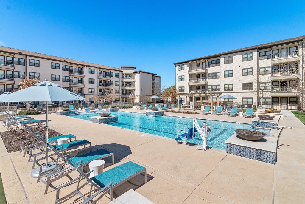 an outdoor pool with lounge chairs and umbrellas with apartments in the background