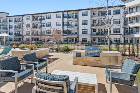 an outdoor patio with chairs and a fire pit in front of an apartment building
