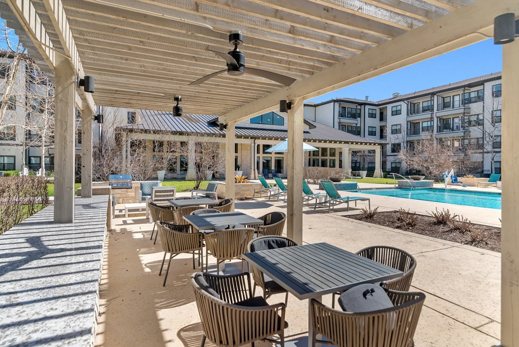 a covered patio with tables and chairs next to a swimming pool