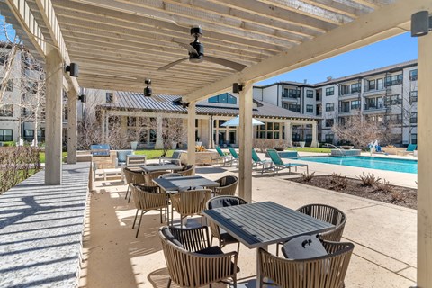 a covered patio with fans, tables and chairs next to a resort-style pool at a senior apartment community