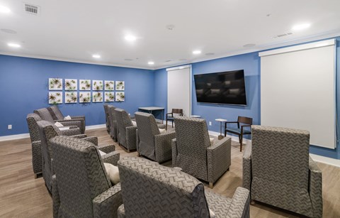a media room with lounge chairs and a large television at a senior apartment community