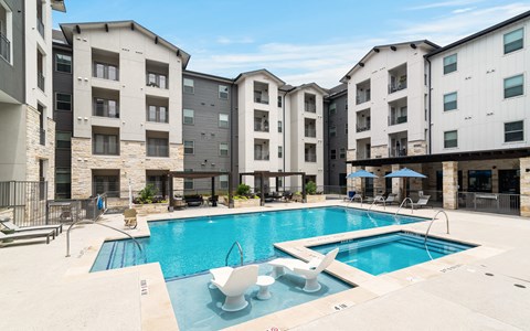 a resort-style swimming pool with lounge chairs and sitting areas covered by a wooden pergola at a senior apartment community