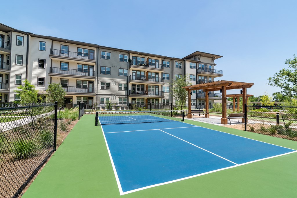 an outdoor tennis court with an apartment building in the background