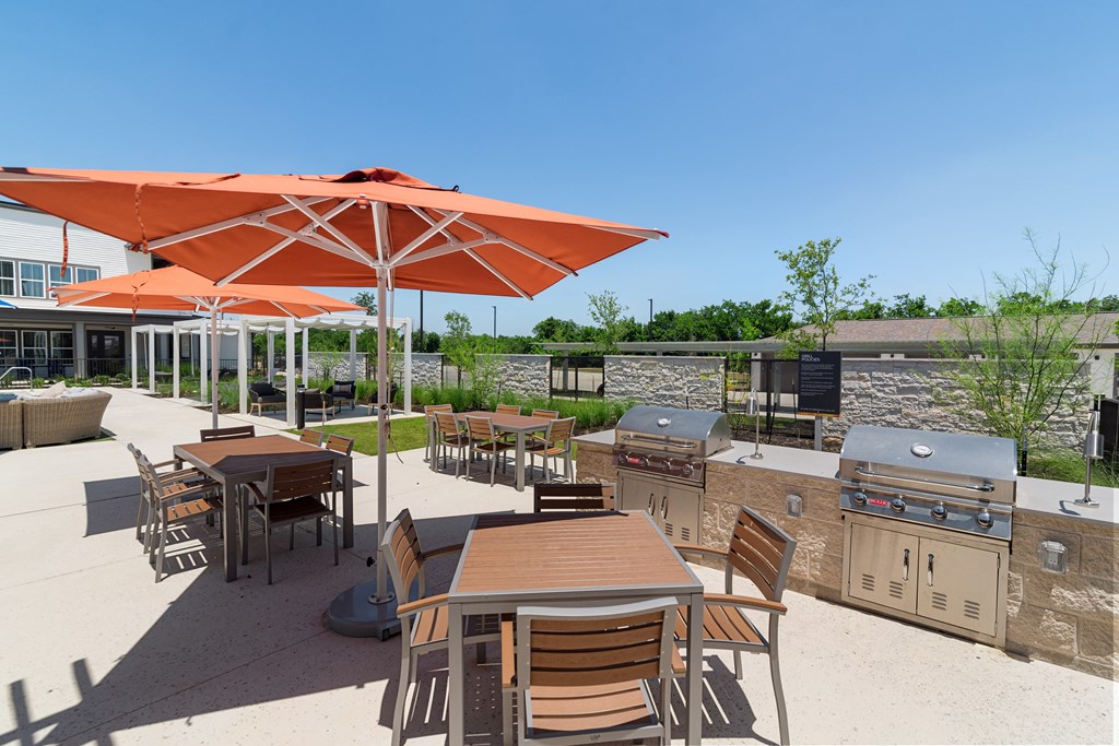 a patio with tables and umbrellas and barbecue grills