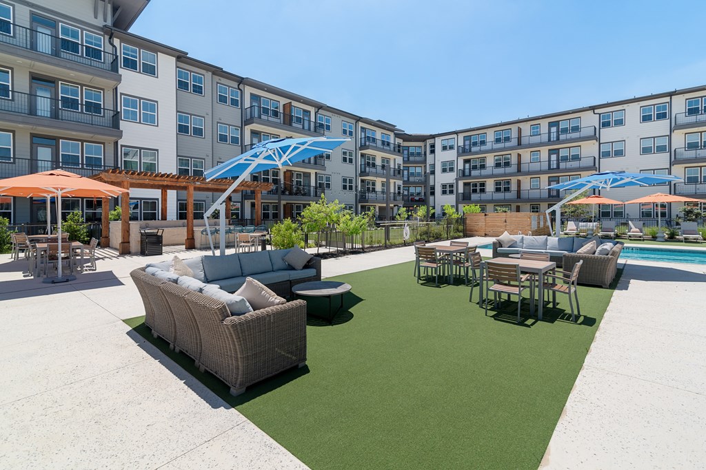 an outdoor lounge area with couches and tables in front of an apartment building