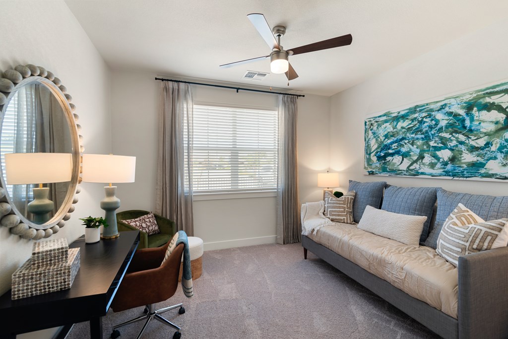 A living room with a grey couch, a desk with a chair, a mirror, and a painting on the wall.