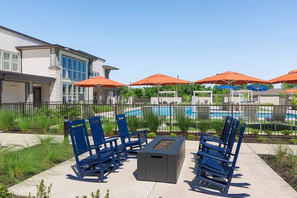 a patio with blue chairs and umbrellas next to a pool