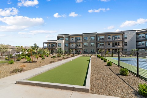 Apartment complex with a green lawn and tennis court.