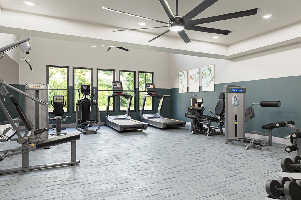 a gym with cardio equipment and windows and a large ceiling fan at a senior apartment community