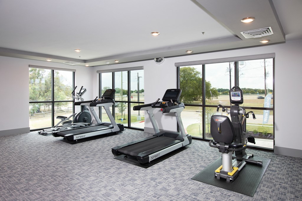 a gym with fitness machines and tall windows at a senior apartment community