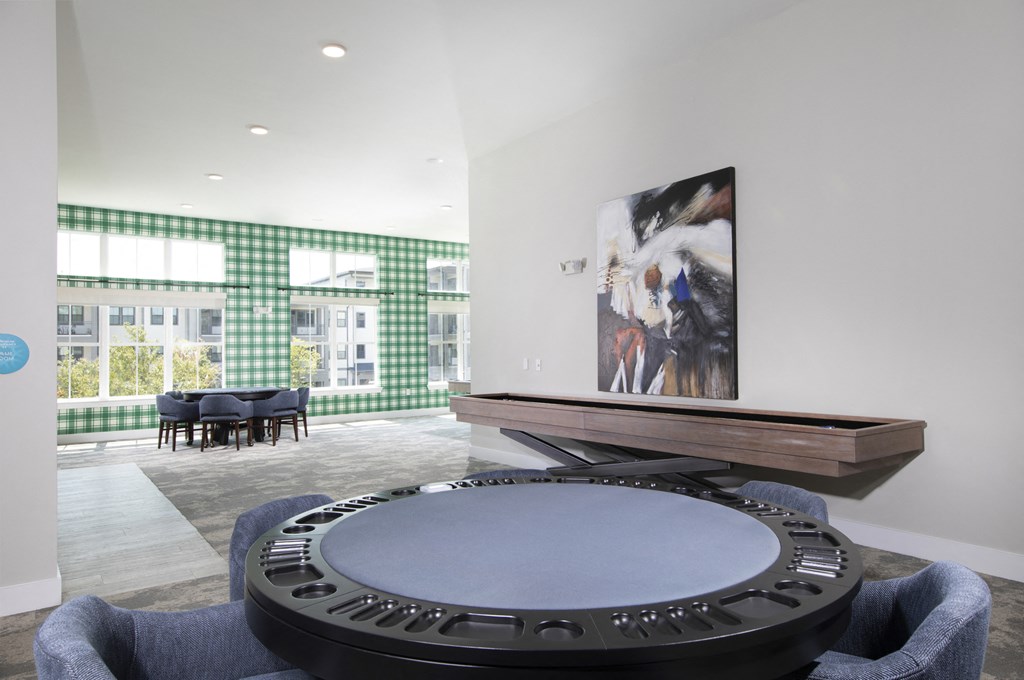a game room with a table shuffleboard and card table with chairs at a senior apartment community