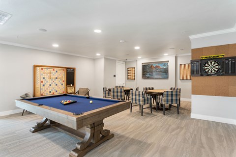 a game room with a pool table and card tables with chairs at a senior apartment community