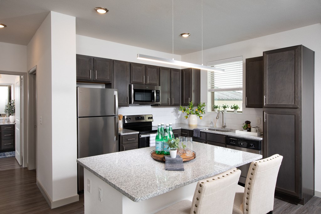 a kitchen with stainless steel appliances, granite countertops and island with chairs at a senior apartment community