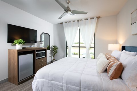 a bedroom with a queen-sized bed, ceiling fan, and windows at a senior apartment community
