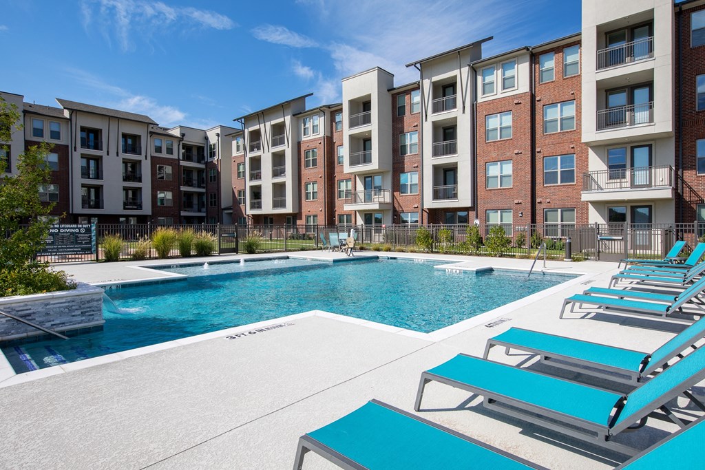 a swimming pool with lounge chairs in front of an apartment building