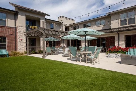 a patio with tables and chairs under an umbrella at a senior apartment community