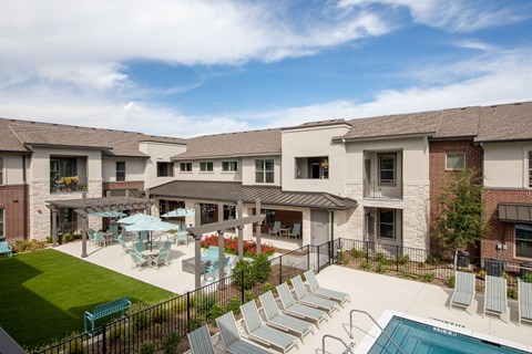a resort-style pool with lounge chairs and patio seating under umbrellas at a senior apartment community