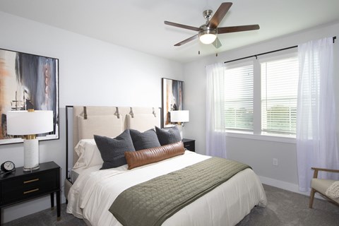 a bedroom with a queen-sized bed, ceiling fan, and windows at a senior apartment community