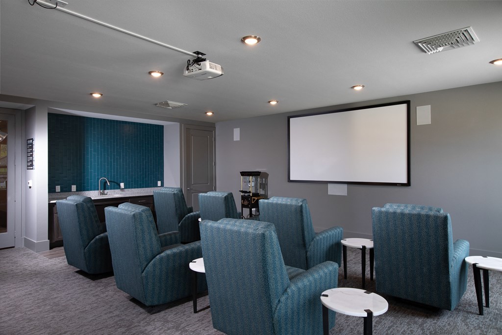 a media room with big chairs and a screen at a senior apartment community