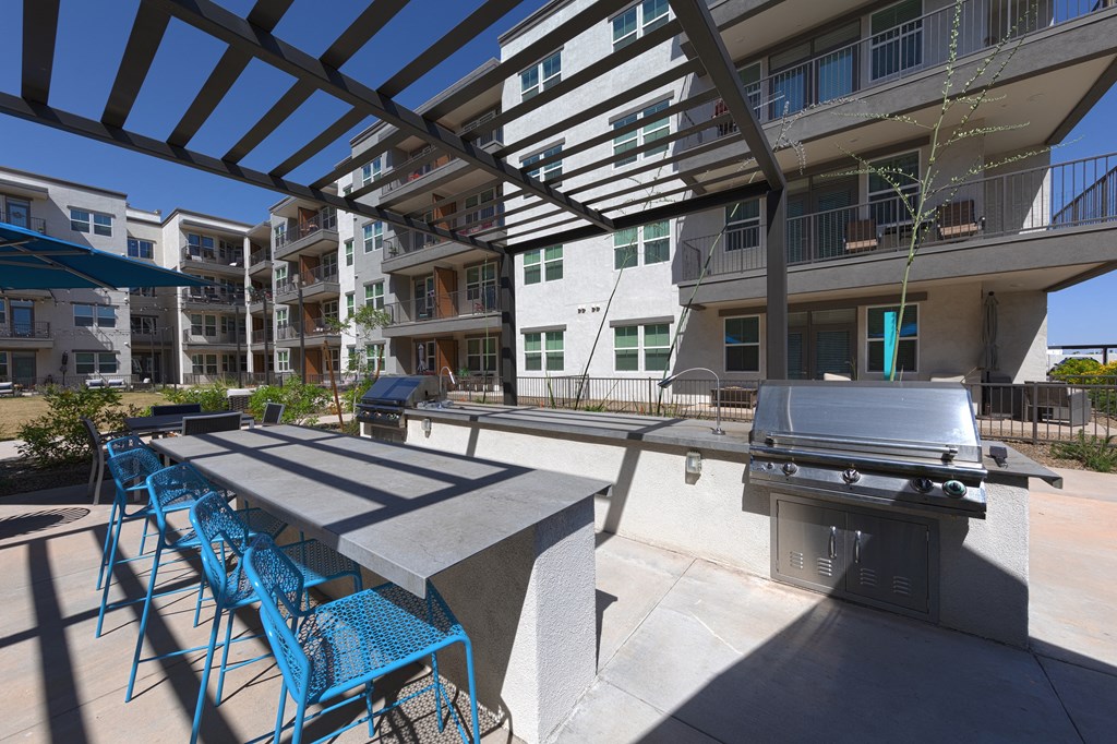 a covered, outdoor grilling station with an island and chairs at a senior apartment community