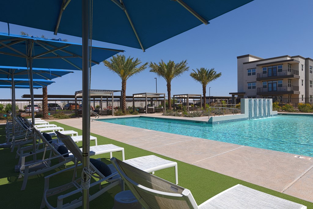 a resort-style pool with lounge chairs and umbrellas at a senior apartment community