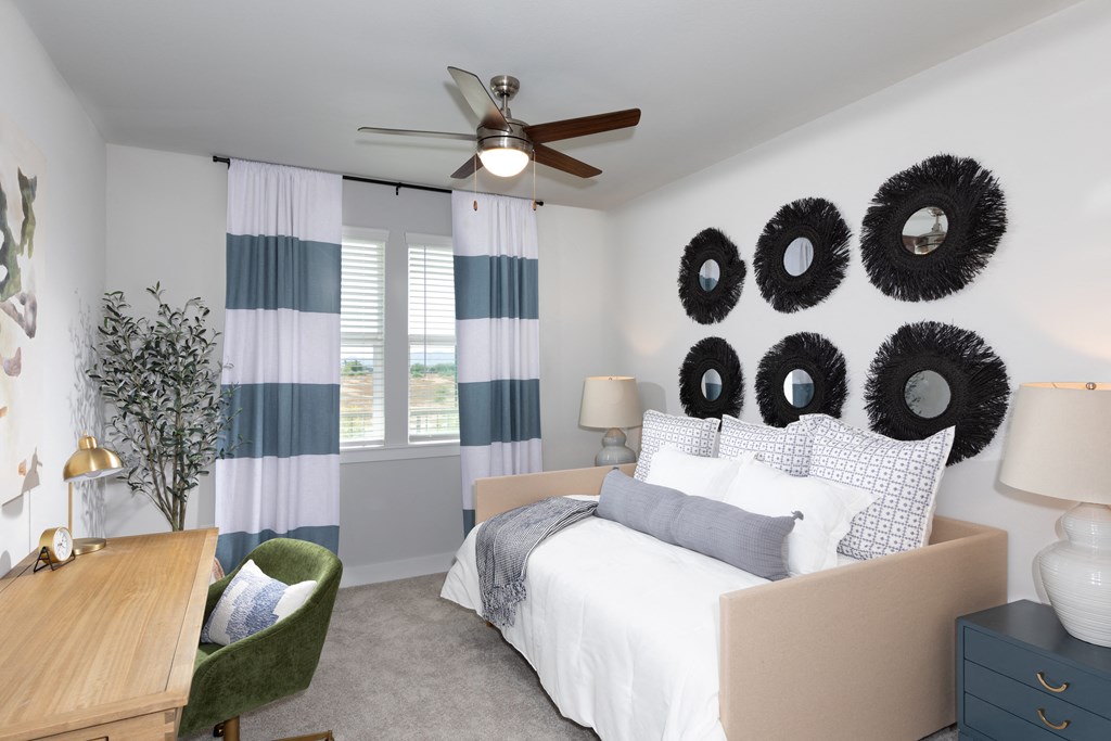 a bedroom with a daybed, desk, and ceiling fan at a senior apartment community